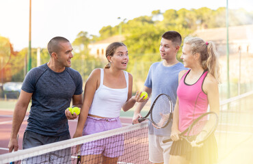 Four smiling sportsmens men and women with rackets emotionally talking and laughing at court