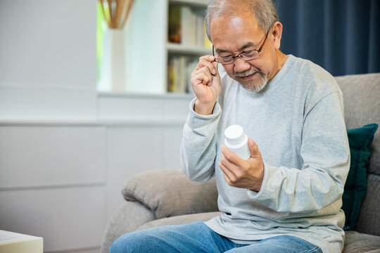 Asian worried senior man with medicine pills he read on see how to take pills before taking, old man buy herbal self cure Rx pill online from pharmacy, home isolation, Medical service concept
