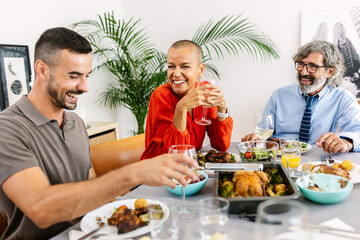 Group of diverse people having lunch together at home. Multi-generational european family having fun gathered around dinning table, laughing and enjoying meal.