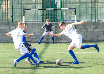 Fototapeta premium Game moments of football match between two teams of teenagers in white and blue shirts