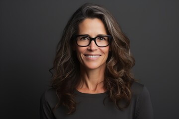 Portrait of a smiling businesswoman with glasses over dark background.