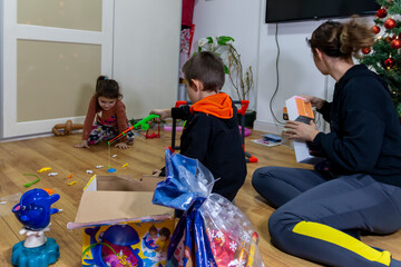 Merry Christmas and Happy New Year! Beautiful mom and her children  are smiling while opening Christmas presents. Christmas gift, presents for New Year.