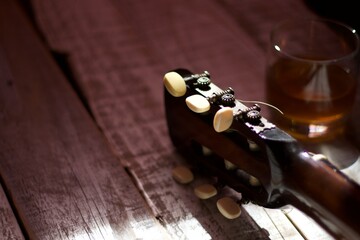 headstock of an acoustic guitar next to a glass of alcoholic beverage, on aged white wood,...
