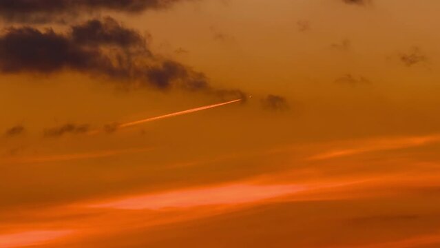 Orange luminosity jet from high altitude airplane at sunset sky