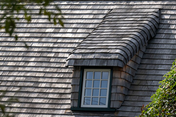 A steep roof of a vintage building with cedar wood shingles. There's a long dormer covered in...