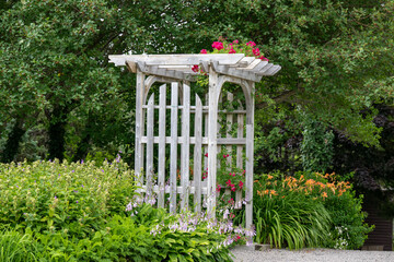 An outdoor wooden curved shaped archway or arbor surrounded by a lush green garden.  The park has...