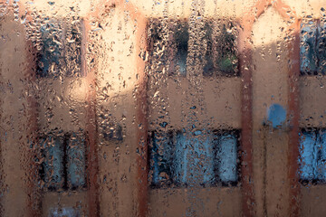 Condensation droplets on the interior of a single pane window with red brick apartment building...
