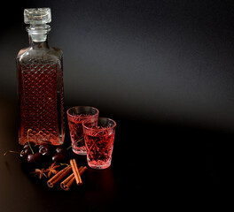 Cherry liqueur with spices on a black background, homemade berry alcohol with cinnamon and anise in...