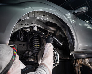An auto mechanic applies anti-corrosion mastic to the underbody of a car.