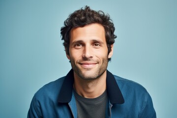 Portrait of a handsome young man smiling at camera against blue background - obrazy, fototapety, plakaty