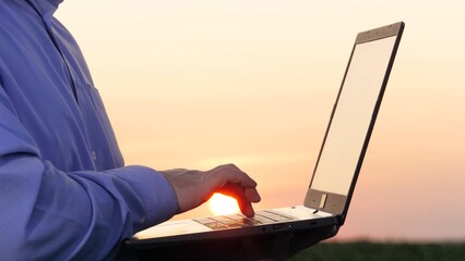 Agriculturist uses keyboard on laptop on corn field closeup. Skilled farmer cultivates corn using computer technology on rural land. Agronomist stores data on laptop while inspecting corn field - obrazy, fototapety, plakaty