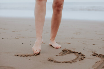 Drawing on the sand with your feet. 
Women's legs. Exercise against flat feet. Foot health.Clean sand. Inscriptions on the sand
