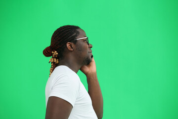 A man in a white T-shirt on a green background talks on the phone, in profile