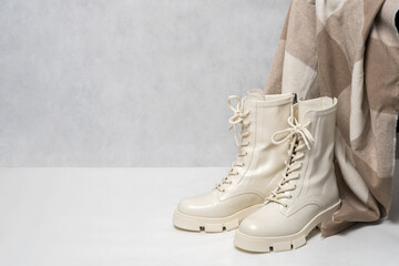Pair of stylish white boots for women and beige winter scarf on light gray background. Trendy...