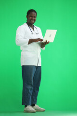 Full-length male doctor typing on a laptop on a green background