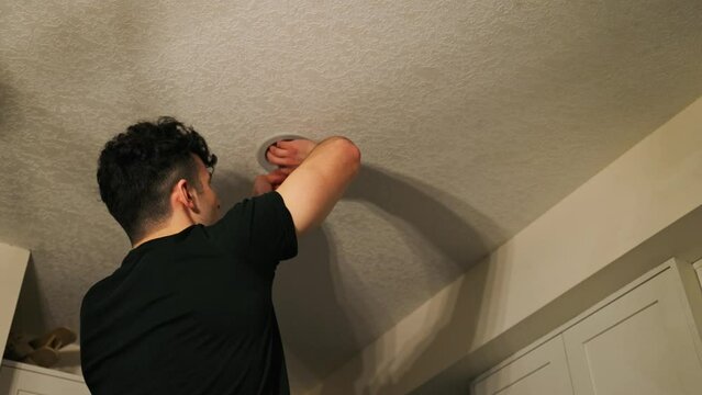 A man on a ladder uninstalls a light bulb