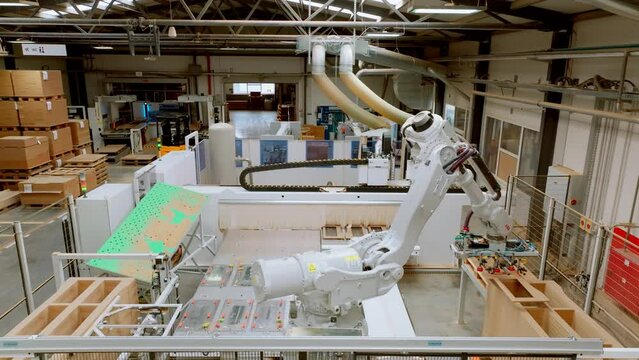 Industrial automation and robotics in modern industrial factory. High precision robotic arm assembling wooden furniture in big furniture manufacturing facility with industrial robotic manipulators.