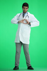 A full-length male doctor shows a heart sign on a green background