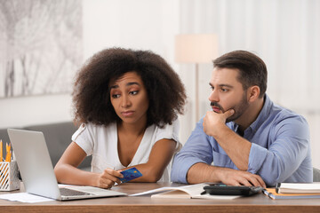 Confused couple with credit card using laptop for planning budget at home. Debt problem