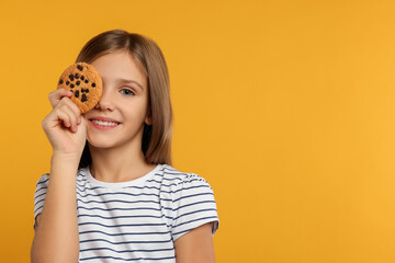 Cute girl with chocolate chip cookie on orange background. Space for text