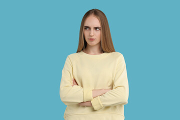 Resentful woman with crossed arms on light blue background