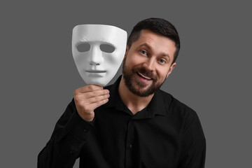 Multiple personality concept. Happy man with mask on grey background