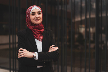 Portrait of a young happy Muslim business woman in hijab near the modern office building. - obrazy, fototapety, plakaty