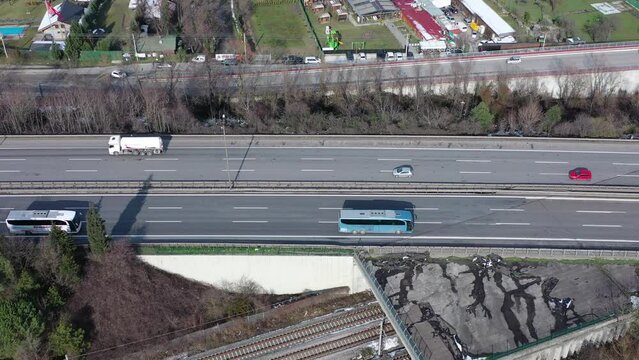 Two-way, multi-lane highway traffic along  Sapanca Lake on a winter morning. Intercity Buses traveling rapidly. Drone follows highway by filming it from the side. Green gardens on both sides 
