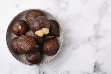 Fresh salak fruits in bowl on white marble table, top view. Space for text