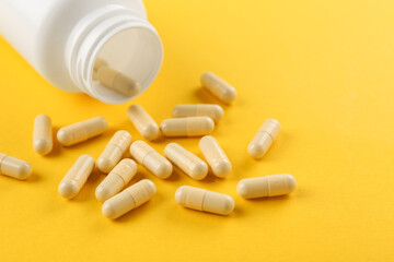 Bottle and vitamin capsules on yellow background, closeup