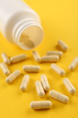 Bottle and vitamin capsules on yellow background, closeup