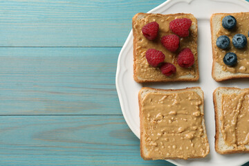 Delicious toasts with peanut butter, raspberries and blueberries on light blue wooden table, top view. Space for text