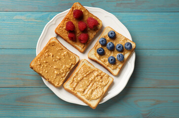 Delicious toasts with peanut butter, raspberries and blueberries on light blue wooden table, top view