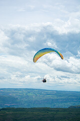 A person paragliding in the sky with a colorful parachute and safety harness.Mountains, Extreme sports in a cloudy day 