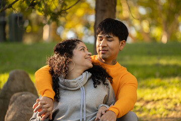 Latin couple hugging and flirting in an urban park sitting in the grass and looking each other