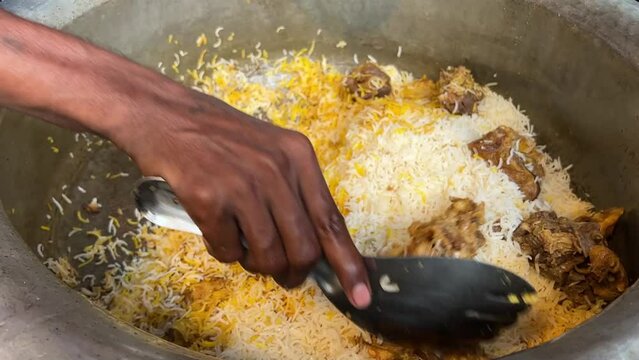 Close up shot of male hands packing hot freshly cooked biryani dish from large container in a kitchen.