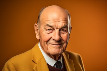 Portrait of a senior man in a yellow jacket on a orange background.