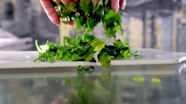 Close-up of hands woman skillfully chopping coriander. High quality Woman's hands raise chopped cilantro or parsley over the table sprinkling, looking through delicious leaves of greenery