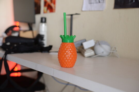 Copo de abacaxi laranja com canudo verde, utensilio de cozinha ex&oacute;tico em cima da bancada 