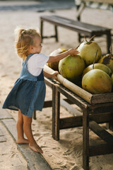 Back view little girl child taking drink coconut while vacation on the bach. Baby buy coconut...