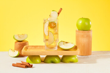 Front view of a wooden tray placed on evenly arranged apple halves. A glass of detox water stands out on a yellow background. Apples provide a lot of vitamin C for the body.