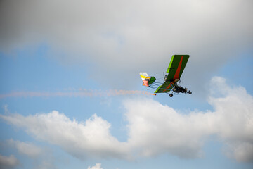 Stunt plane leaves smoke trail in aerobatic performance against blue sky. Skilled pilot maneuvers...