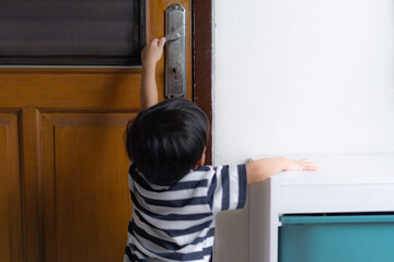 Fototapeta na wymiar curious toddler kids trying to pull the door handle to open the wooden door