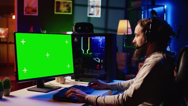 Man having fun by using green screen computer monitor to play singleplayer videogame. Professional gamer using mockup PC desktop to complete levels in game, talking with friends