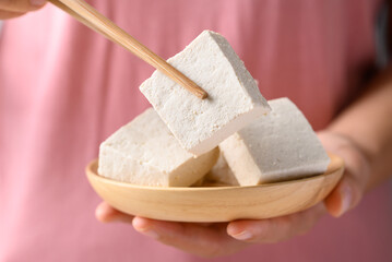 Fresh tofu in wooden bowl with hand holding chopsticks, Vegan food ingredient in Asian cuisine, Plant based diet
