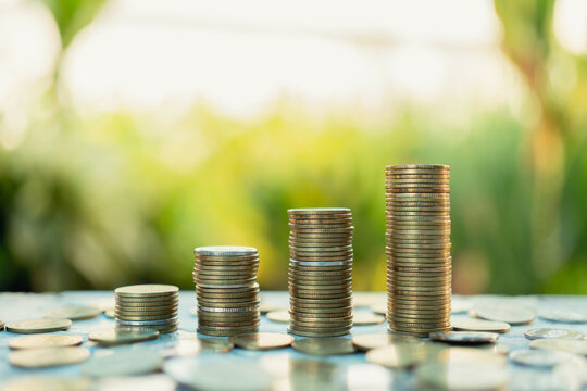 Investment concept, stacked coins on the table, background of green trees and sunset light.