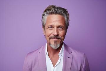 Portrait of handsome mature man with grey hair and beard looking at camera while standing against purple background