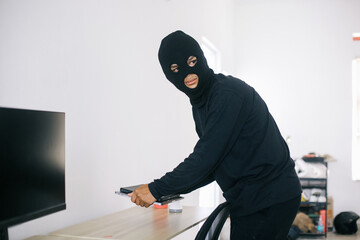 Bad and sneaky thief with black clothes and balaclava stealing laptop from house. Crime and...