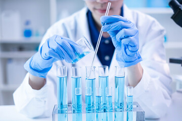 Woman research scientist biology chemistry medicine pouring liquid from beaker to test tube indoor science laboratory room, adult female person blue glove work discovery experiment medical chemist