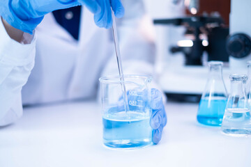 Closeup scientist hand using stirring rod for stirring blue liquid solution glass beaker chemical...